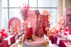 a room filled with tables and chairs covered in pink, white and red balloons next to a window