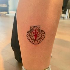 a woman's leg with a small tattoo on the side of her body, depicting a shell and a red cross