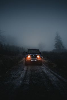 a jeep driving down a dirt road in the middle of the night with fog on it