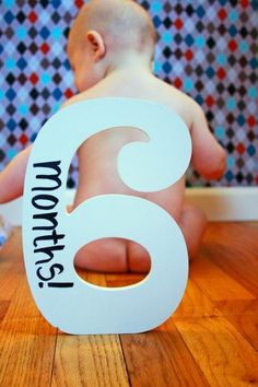 a baby sitting on the floor next to a number six sign