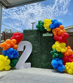 the number two is made out of balloons and placed in front of a wall with grass