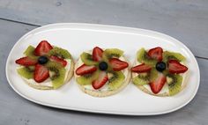 three small sandwiches with fruit on them are arranged on a white plate, ready to be eaten