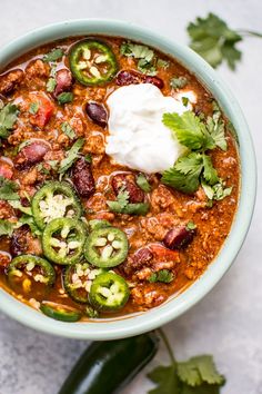 a bowl of chili soup with sour cream and jalapenos on the side