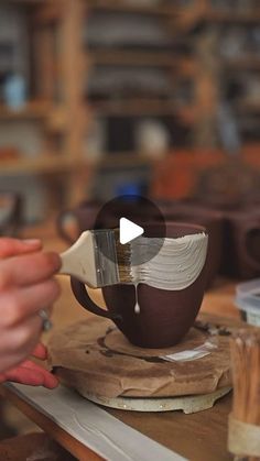 a person holding a spoon over a cup on top of a wooden table in a workshop