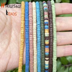 four different colors of bracelets are held in someone's hand with green leaves behind them