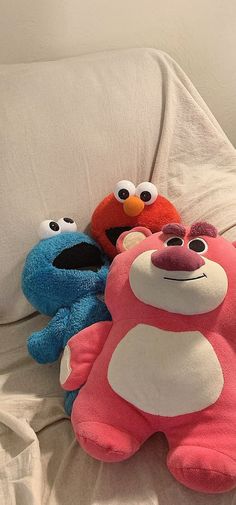 three stuffed animals sitting on top of a bed next to each other, with eyes wide open