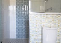 a white toilet sitting in a bathroom next to a walk in shower and tiled walls