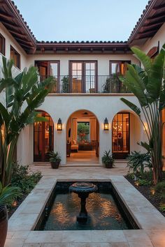 a courtyard with a fountain and potted plants in front of the house at dusk