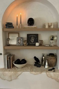 a shelf filled with books and candles on top of a white wall next to a bowl