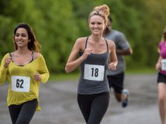 three women running in a race with numbers on their vests and one has her thumb up