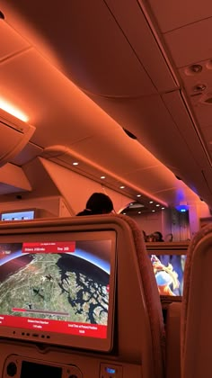 the inside of an airplane with two televisions on it's back and people watching