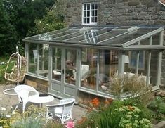 a house that has a glass roof and some chairs in the front yard with flowers around it