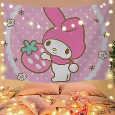 a hello kitty wall hanging on the side of a bed with fairy lights around it