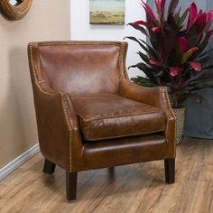 a brown leather chair sitting on top of a hard wood floor next to a potted plant