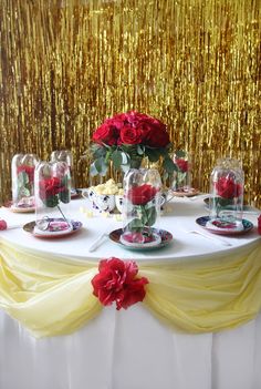 a table topped with plates and vases filled with red roses next to a gold curtain