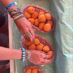 two women are holding oranges in baskets on a table with other people's hands