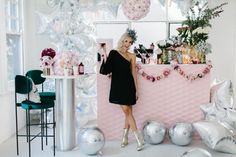 a woman standing in front of a pink bar with balloons and decorations on the wall