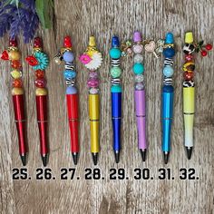 several different colored pens sitting next to each other on a wooden table with flowers and beads