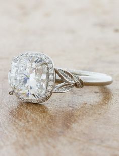 an old - fashioned diamond ring sits on a wooden surface, with the center stone surrounded by filigrees