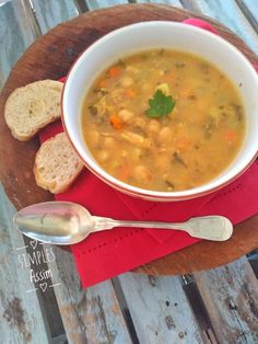 a bowl of soup and two slices of bread on a wooden board with a spoon