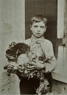 an old black and white photo of a young boy holding lettuce in his hands