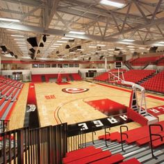 an empty basketball court with red seats and railings on each side, in the middle of a gym