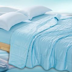 a bed with blue sheets and pillows on top of it, next to an ocean scene