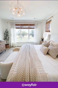 a large white bed sitting under a chandelier in a bedroom next to a window