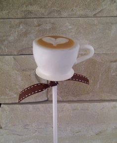 a coffee cup on top of a white stick with a brown bow around the handle