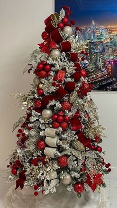 a christmas tree with red and silver ornaments on it's base, in front of a cityscape