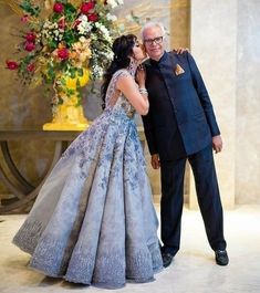 an older man and young woman dressed in formal wear standing next to each other with their arms around each other