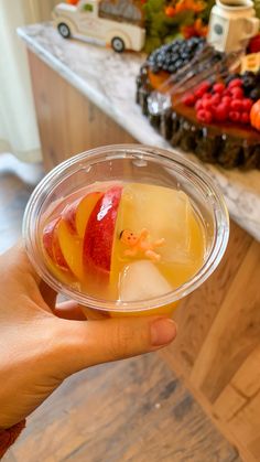 a person holding up a glass with fruit in it on a table next to other fruits