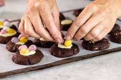 someone decorating cookies with marshmallows and other candies on a baking sheet