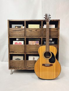 an acoustic guitar sits in front of a bookcase