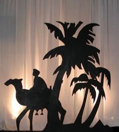 a silhouette of a man riding a camel next to a palm tree