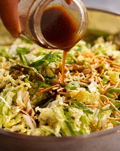 someone adding dressing to a salad in a bowl