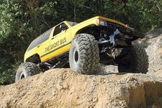 a yellow truck on rocks with trees in the background