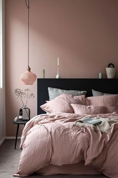 a bed with pink linens and pillows in a room that is painted light pink