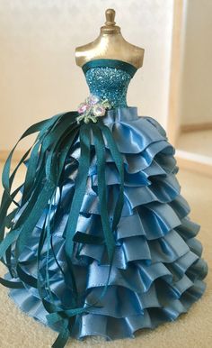 a dress made out of blue ruffled material with flowers on the top and green ribbon at the bottom