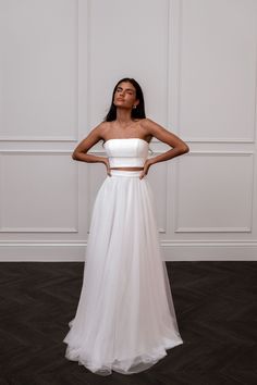 a woman standing in front of a wall wearing a white dress with two pieces on it