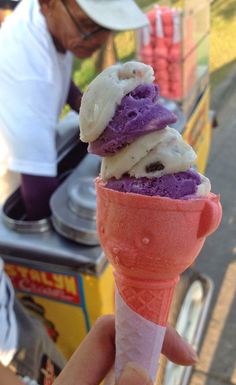 a person holding an ice cream cone with purple and white toppings on it in front of a food cart