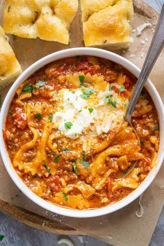 a white bowl filled with pasta and cheese on top of a cutting board next to rolls