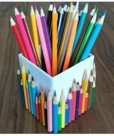 a cup full of colored pencils sitting on top of a wooden table next to an iphone