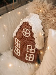 a crocheted gingerbread house pillow on a white couch with christmas lights in the background