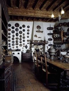 an old fashioned kitchen with many pots and pans on the wall