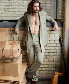 a man with long hair and no shirt standing next to boxes in front of a brick wall