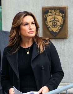 a woman standing in front of a police department building with her arms crossed and looking off to the side