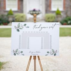 an easel with a wedding seating chart on it in front of a large house