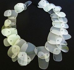 a necklace made out of plastic plates on a black surface with white tags attached to it