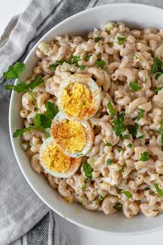 a white bowl filled with macaroni salad topped with hard boiled eggs and parsley